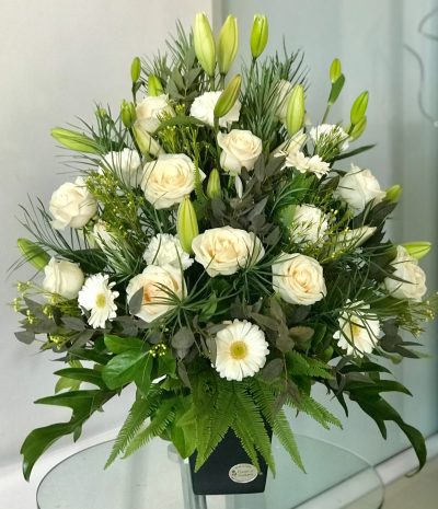 white flower arrangement in black vase with lilies roses and daisies on nude background