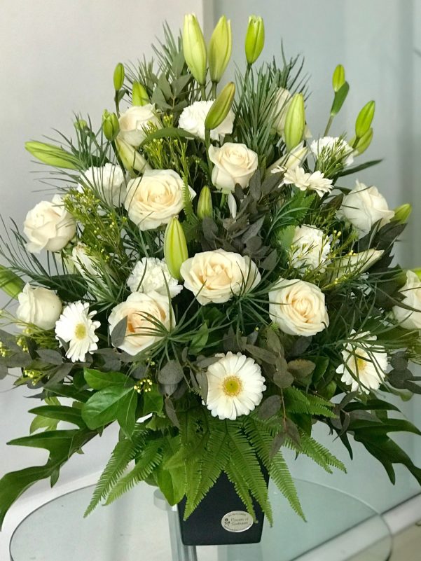 white flower arrangement in black vase with lilies roses and daisies on nude background