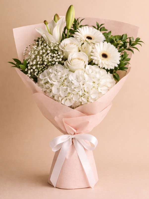 White sympathy bouquet of lilies, roses, gerberas and hydrangea with baby's breath in soft pink wrap.