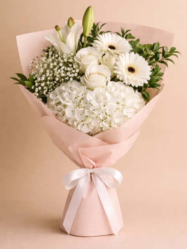 White sympathy bouquet of lilies, roses, gerberas and hydrangea with baby's breath in soft pink wrap.