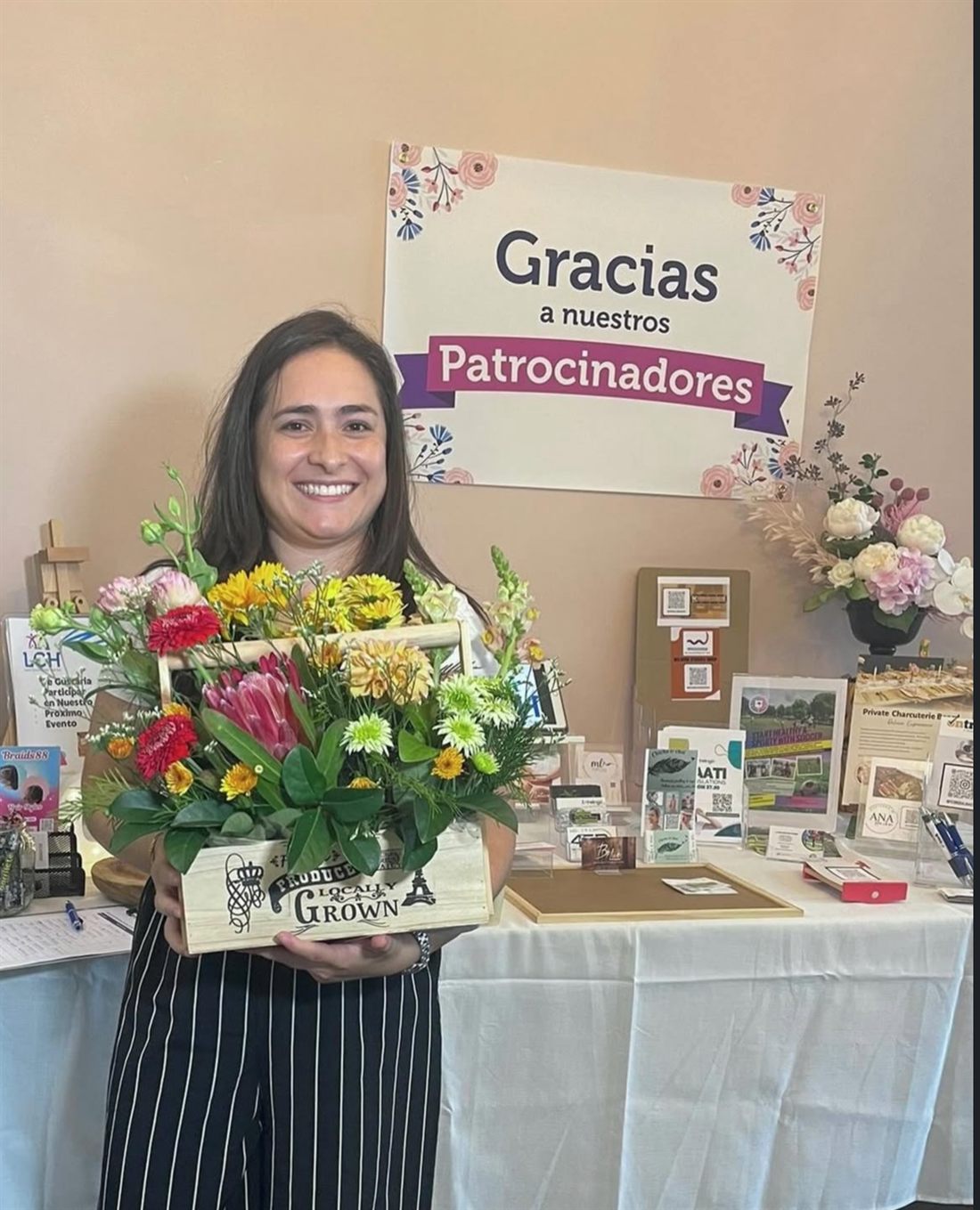 A Flowers of Southport floral arrangement donated as a sponsor for a Latin Community Hub Gold Coast event, held by an LCH organiser in front of the